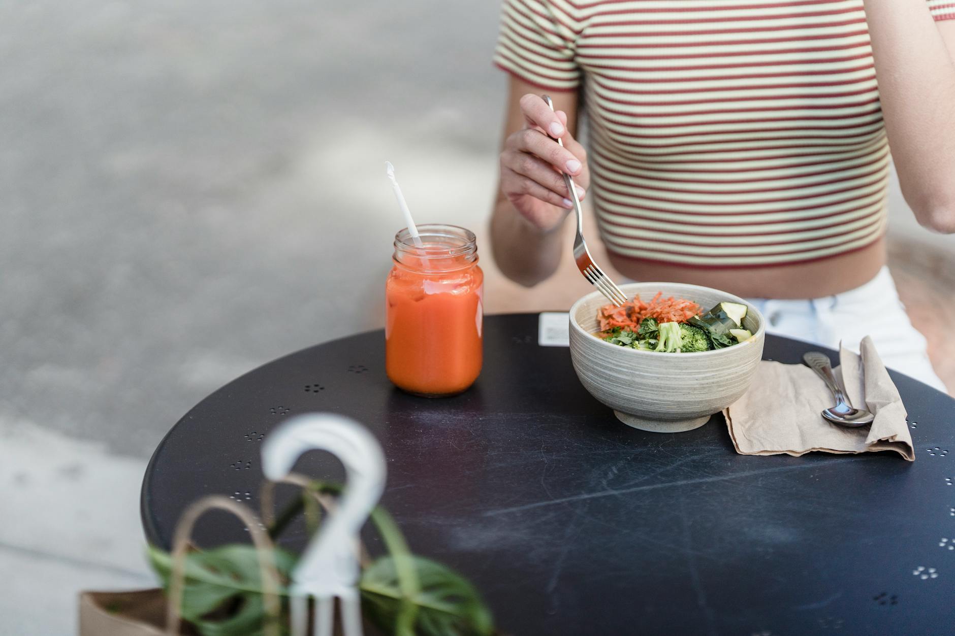 Crop unrecognizable female with bowl of delicious vegetarian salad and jar of refreshing beverage at table in urban cafe